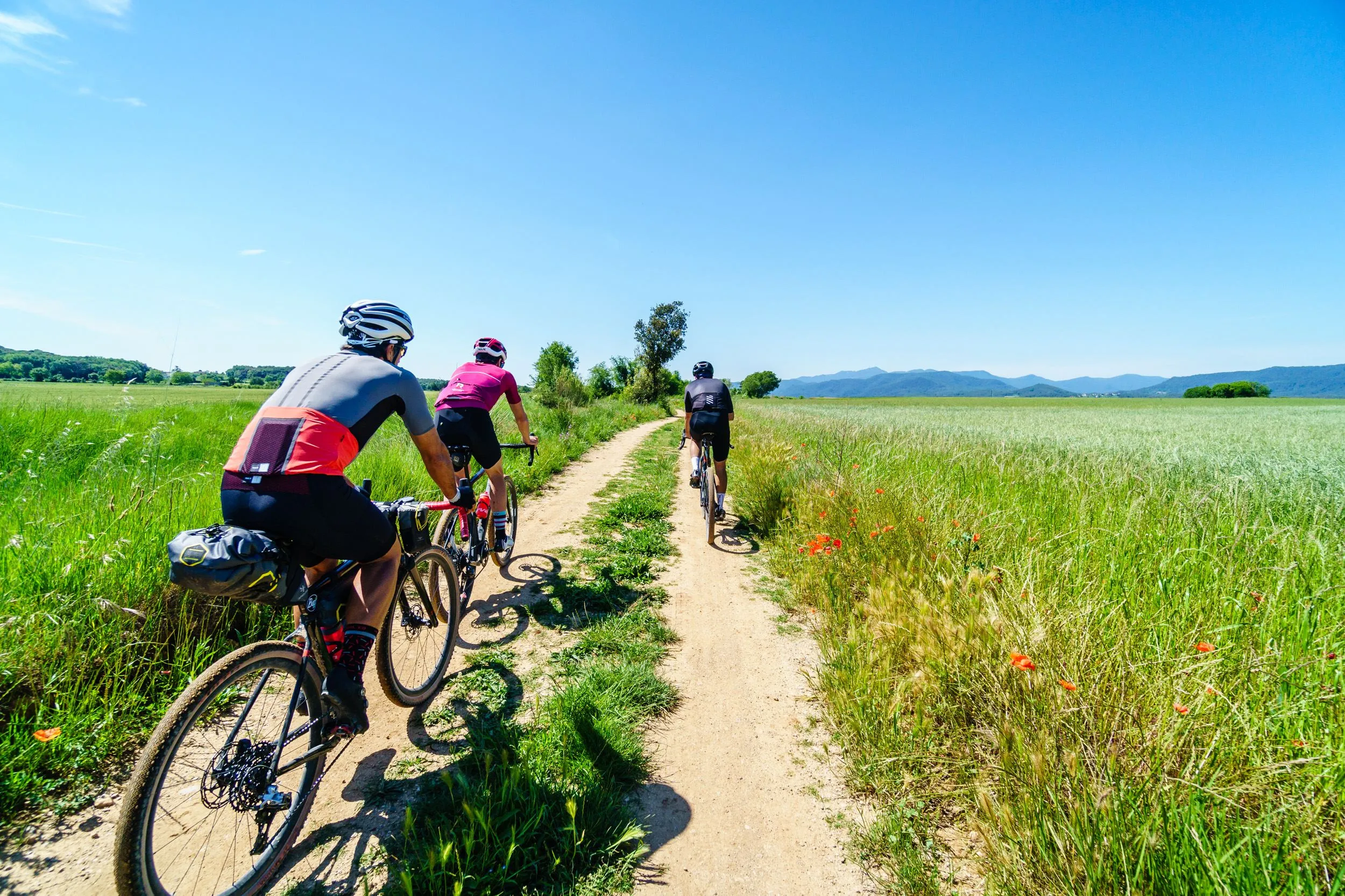 Three cyclists riding a gravel track through green fields outside Girona